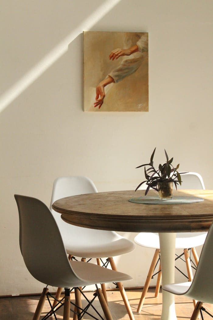 who-we-are-img Sunlit minimalist dining room with round table, chairs, and painting.