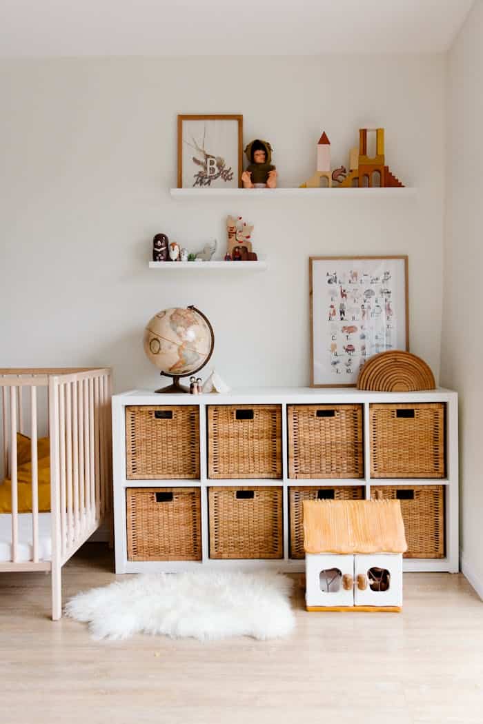our-journey-01 Comfortable bed with toys globe and paintings placed on wooden cabinet with wicker boxes and soft white rug with toy house on floor